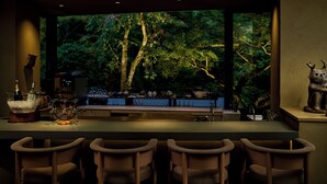 A bar area with a view of a forest through large windows, bar stools, and a variety of glassware and bottles on the counter. - moksa Rebirth Hotel (Kyoto)