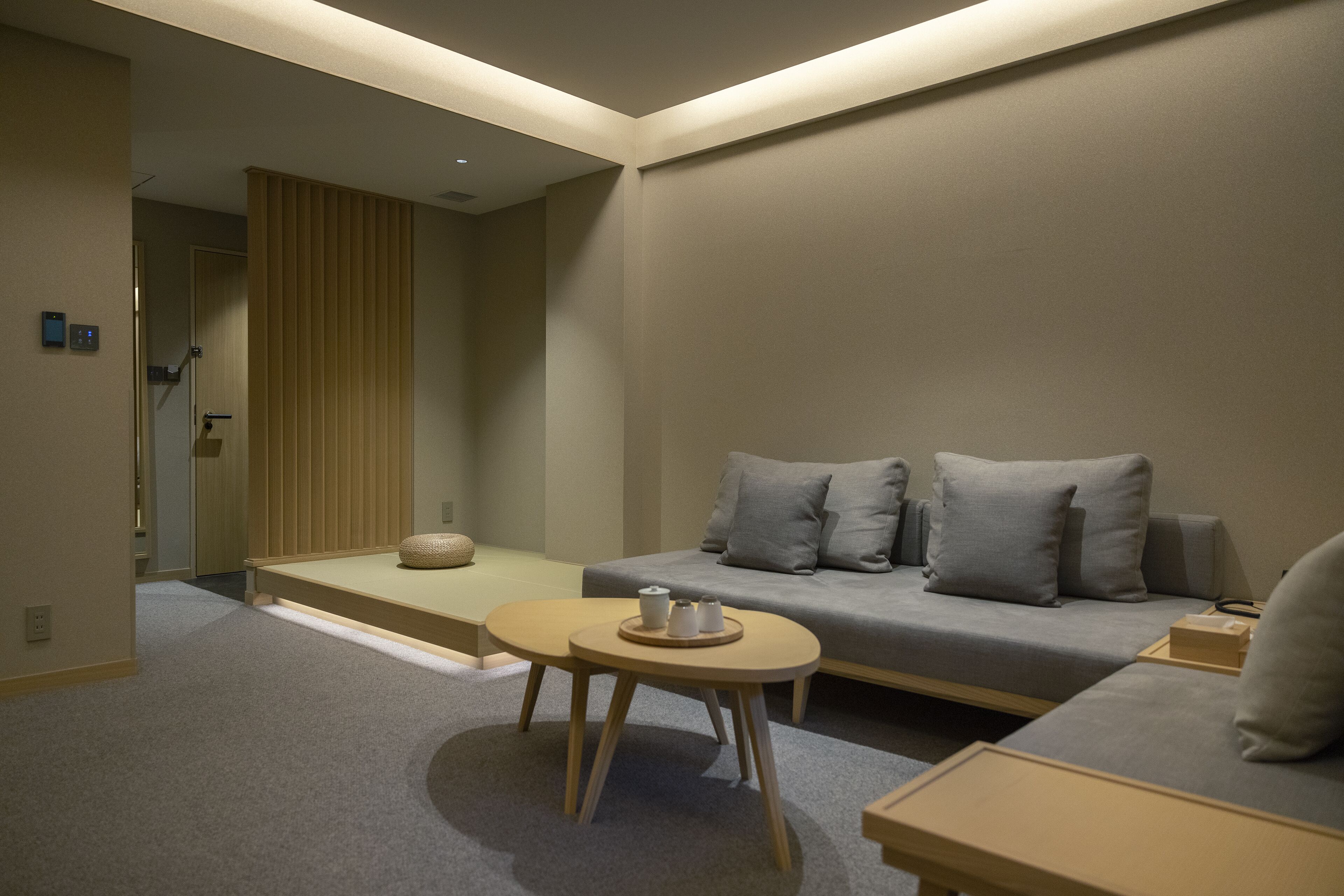 Una habitació d'hotel moderna amb un sofà gris, una taula rodona petita i una banca de fusta.