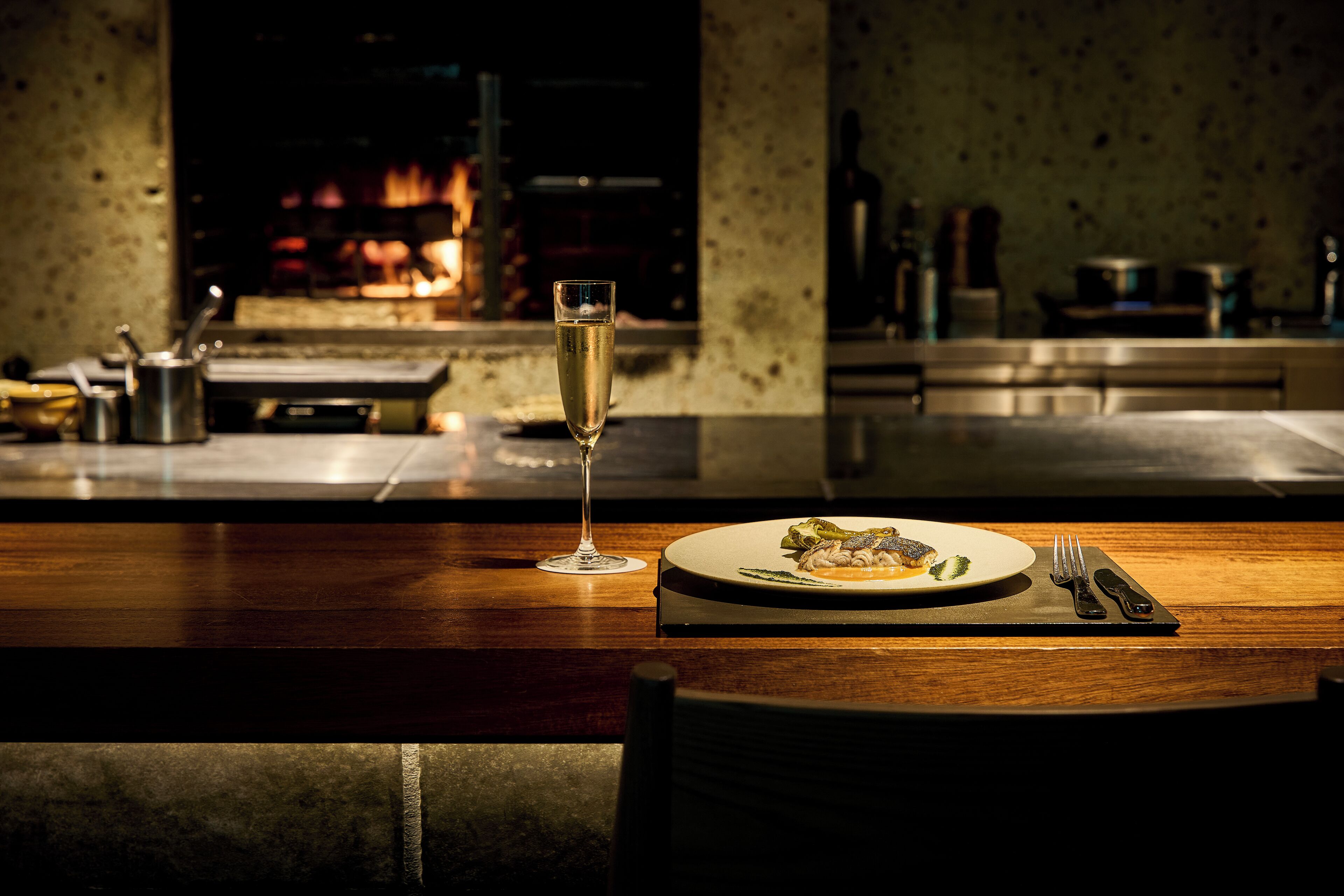A dining table with a plate of food, a glass of champagne, and cutlery.