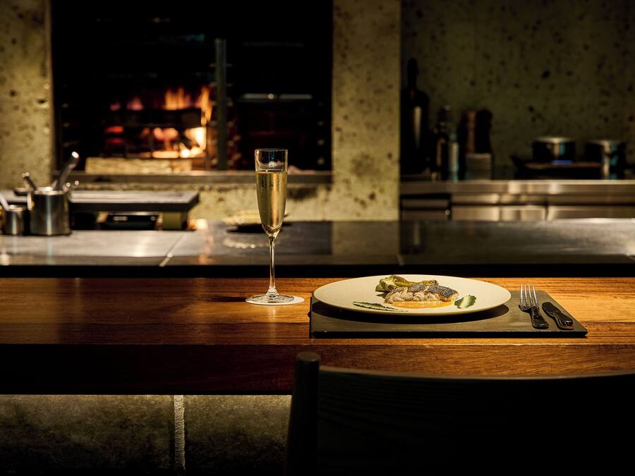 A dining table with a plate of food, a glass of champagne, and cutlery.