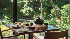 A dining table with breakfast items, a teapot, and a view of a lush garden. - moksa Rebirth Hotel (Kyoto)
