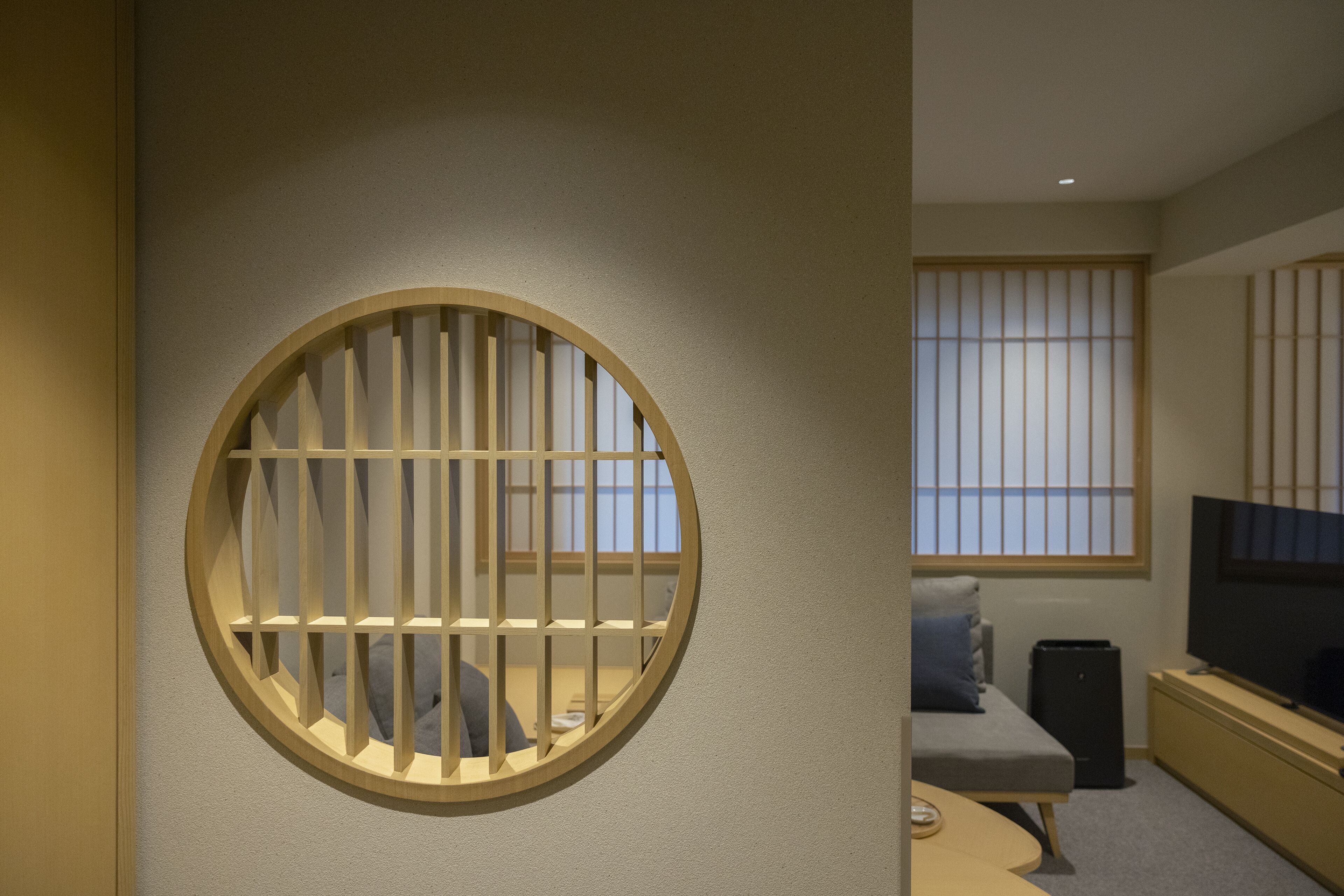 Una habitación con ventanal circular y barrotes verticales, una cama, un televisor y una pequeña mesa.