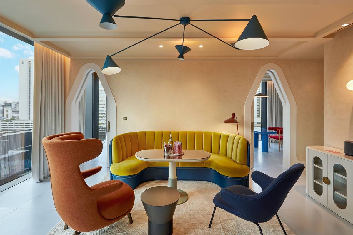 Ein modernes Wohnzimmer mit einem gebogenen gelben Sofa, einem runden Tisch und zwei Stühlen.