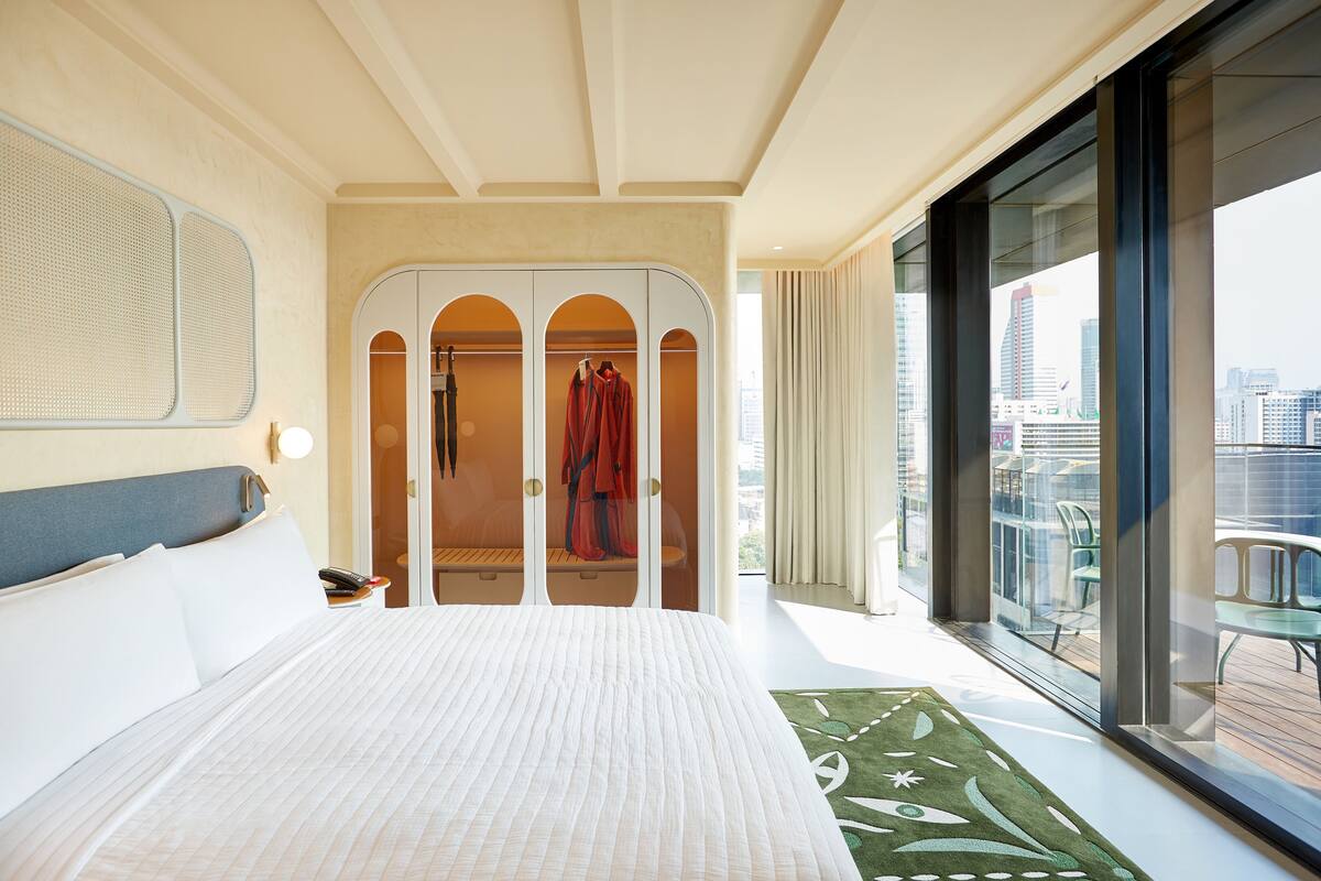 Ein Hotelzimmer mit einem großen Bett, einem begehbaren Kleiderschrank und einem Balkon mit Blick auf die Stadt.
