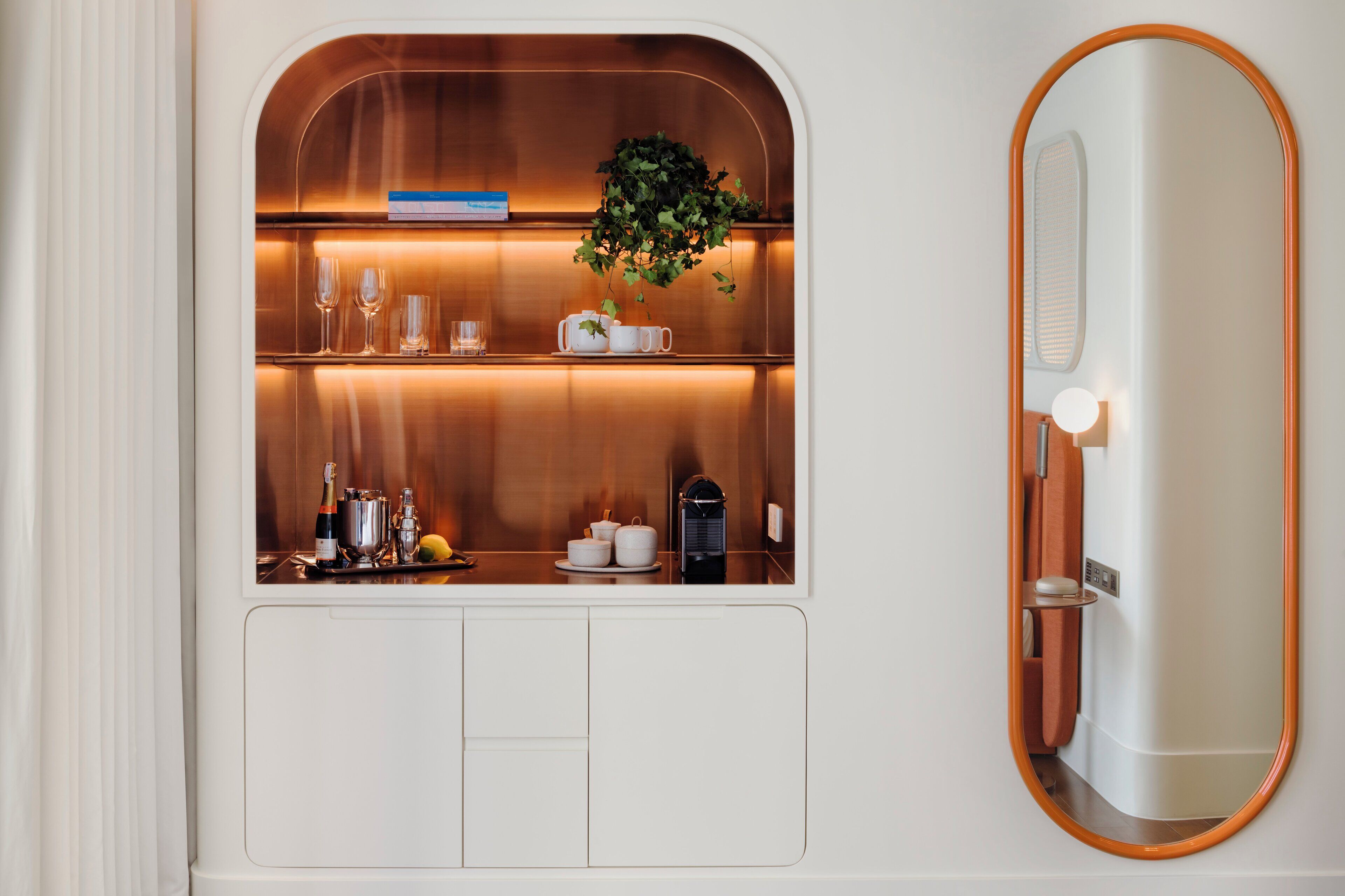 A compact minibar with a mirror, a small plant, and neatly arranged glassware and bottles.