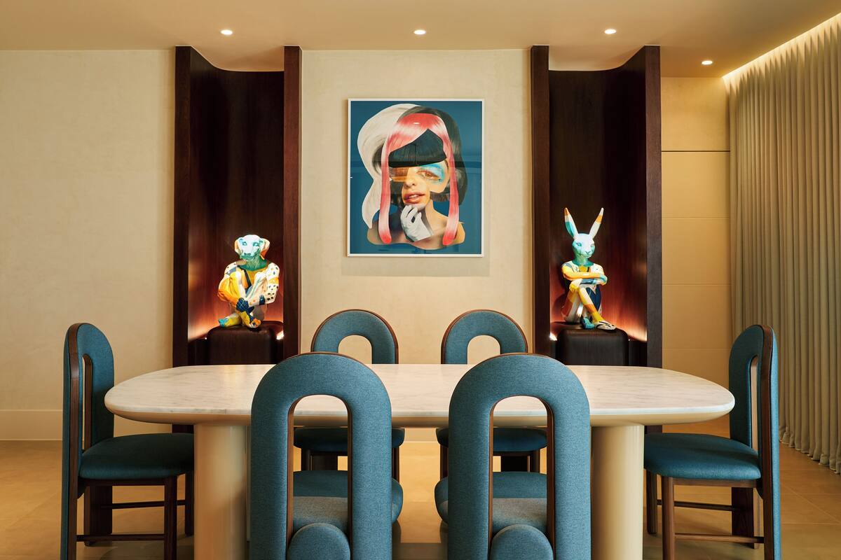 Ein Essbereich mit einem runden Tisch und sechs Stühlen, einem großen gerahmten Kunstwerk an der Wand und je einer dekorativen Statue auf jeder Seite des Tisches.