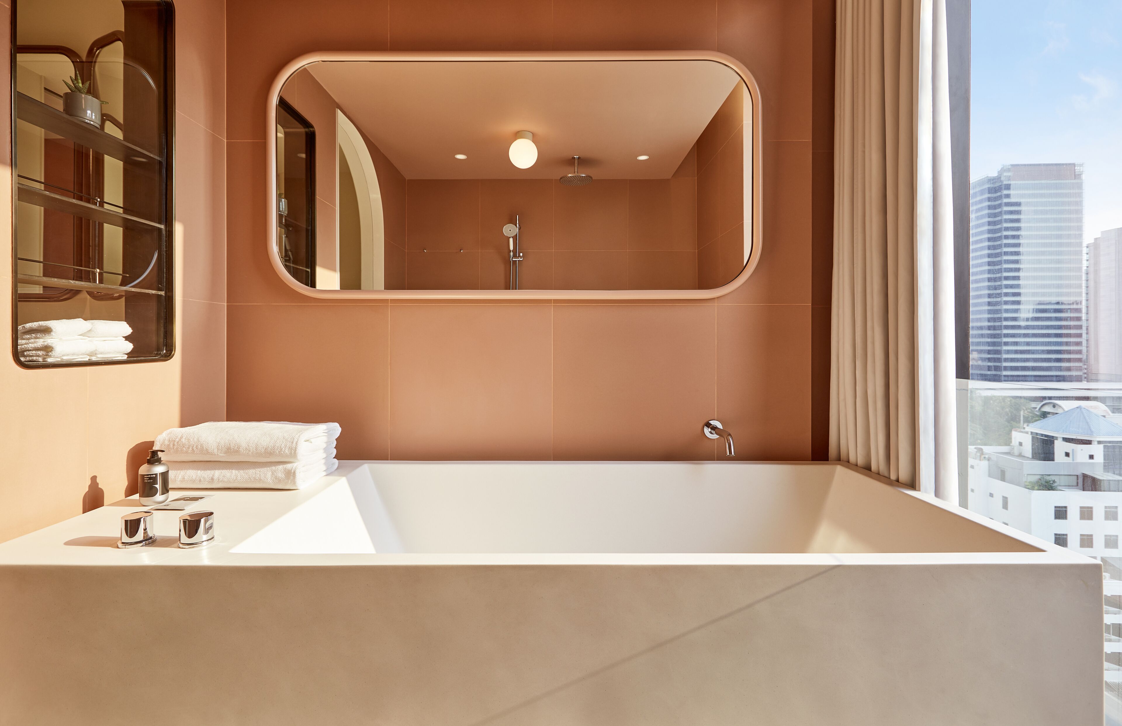 A modern bathroom with a large bathtub, a mirror, and a view of the city.