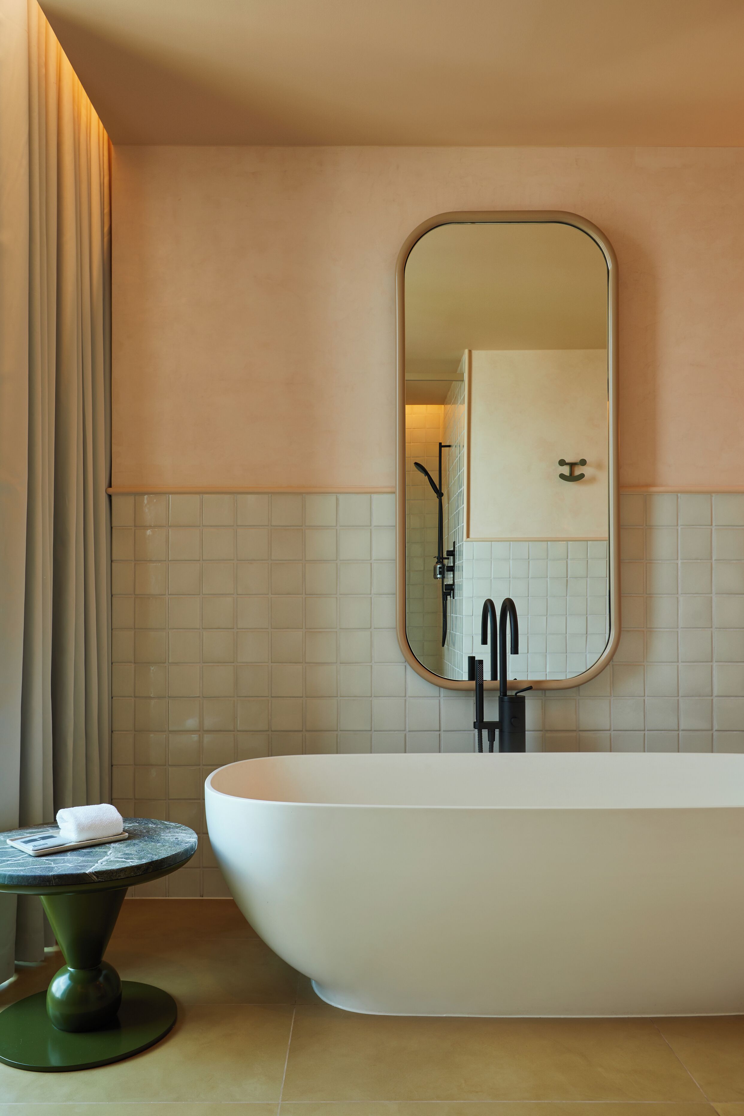 A modern bathroom with a freestanding bathtub, a round mirror, and a small table with a towel.