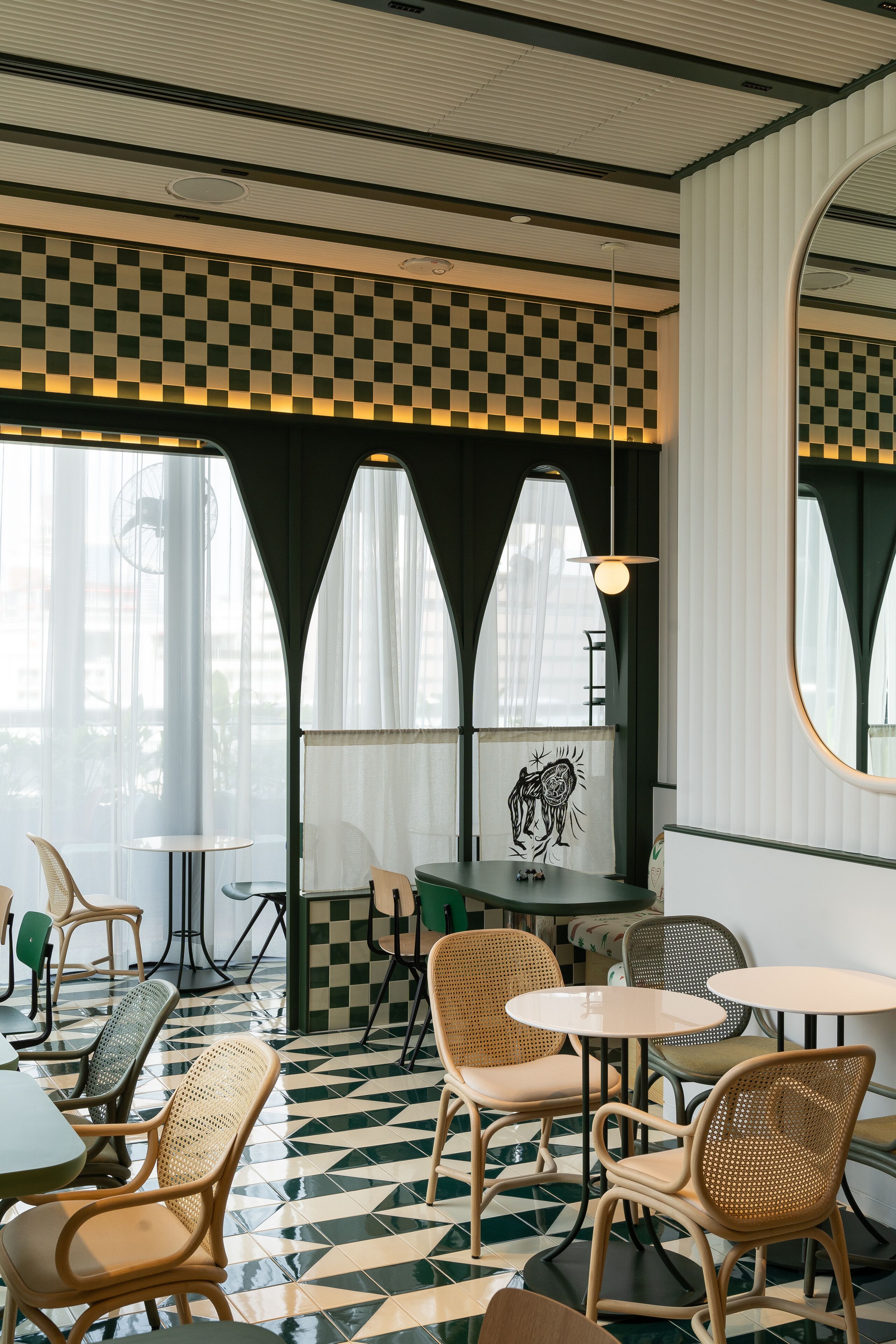 Un café au sol à carreaux, avec des tables rondes et des chaises en osier.