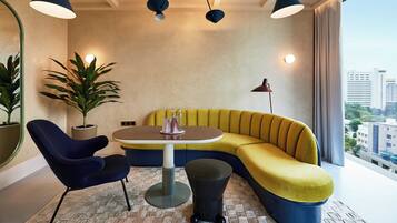 A modern room with a yellow sofa, a round table, and two chairs. There are two potted plants and a floor lamp.