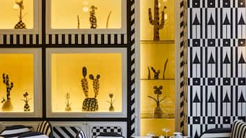 Un comedor con sillas y mesas a rayas negras y blancas, patrones geométricos en la pared y vitrinas iluminadas con esculturas de cactus.
