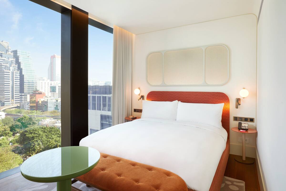 Ein Hotelzimmer mit einem großen Bett, einem kleinen Tisch, Blick auf die Stadt und modernem Design.