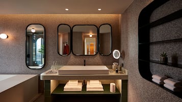 A modern bathroom with a large sink, three mirrors, a vanity with a mirror, and a shelf with towels.
