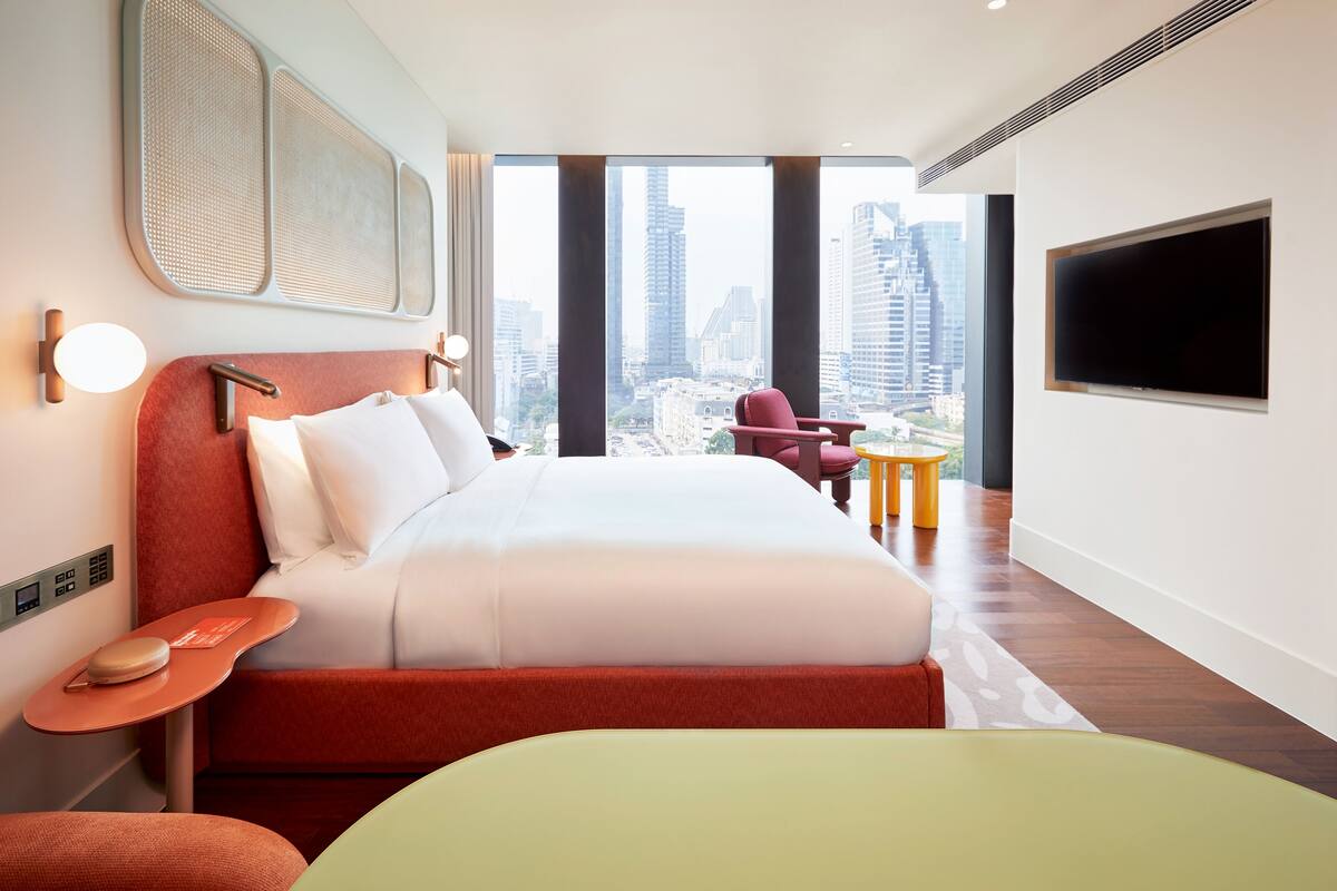 Ein modernes Hotelzimmer mit einem großen Bett, Blick auf die Stadt, einem Flachbildfernseher und einem kleinen Tisch.