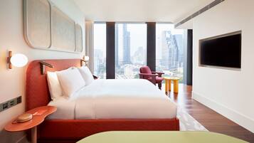 A modern hotel room with a large bed, a city view, a flat-screen TV, and a small table.