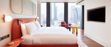 A modern hotel room with a large bed, a city view, a flat-screen TV, and a small table.