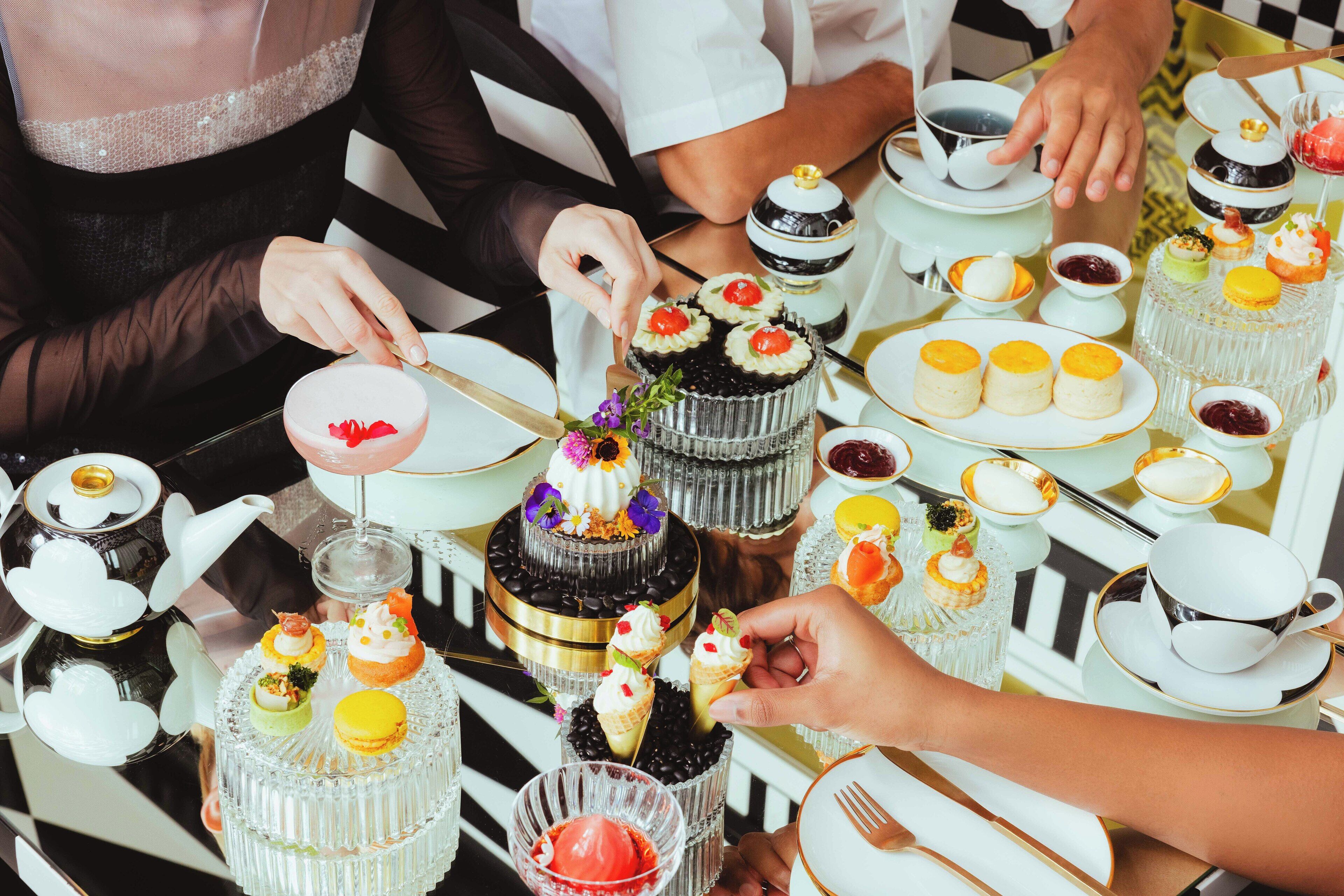 Una mesa dispuesta con diversos postres y servicio de té, incluyendo pasteles, magdalenas y una tetera.