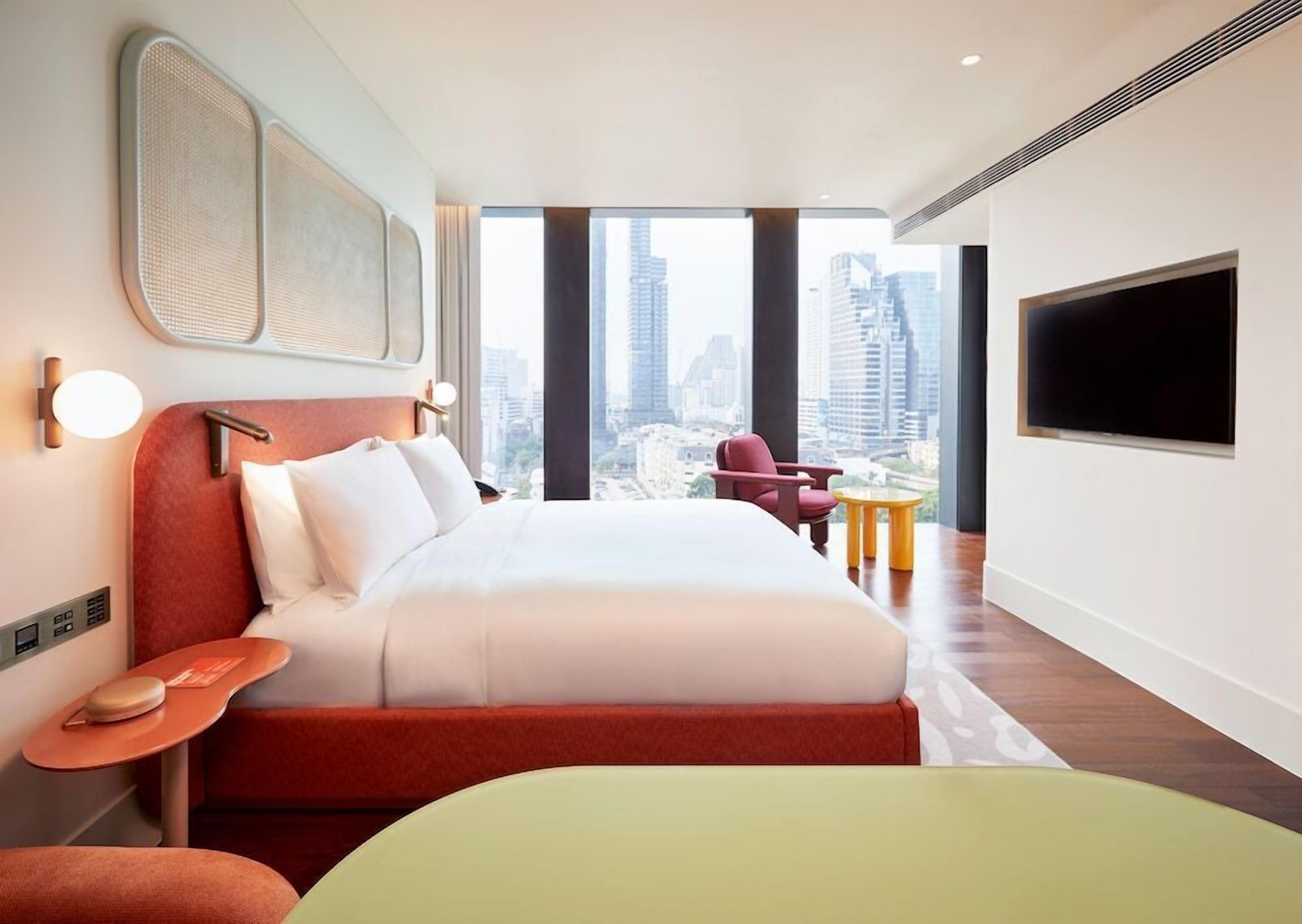 Une chambre d’hôtel moderne avec un grand lit, une télévision, une vue sur la ville et une petite table.