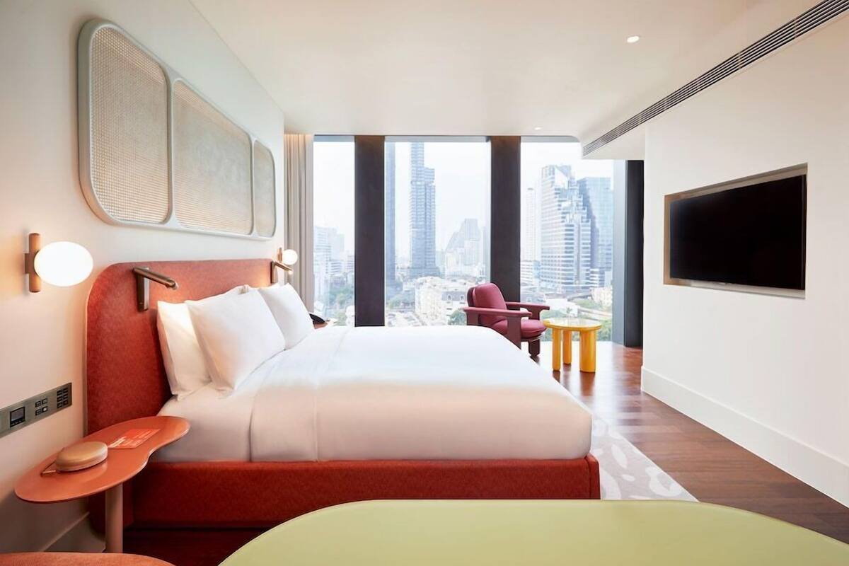 Ein modernes Hotelzimmer mit einem großen Bett, einem Fernseher, Blick auf die Stadt und einem kleinen Tisch.