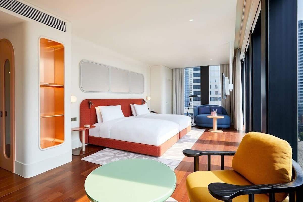 Ein Hotelzimmer mit Bett, Stuhl, kleinem Tisch und Blick auf die Stadt.