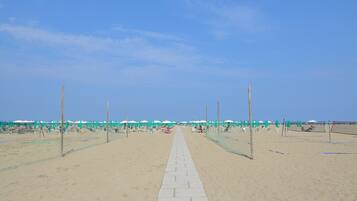 Una passeggiata sulla spiaggia con ombrelloni e lettini, che conduce al mare.