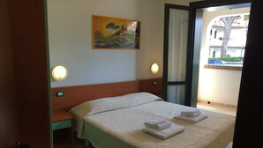 A hotel room with a bed, a painting on the wall, and a view through an open door. - Resort in Lido di Spina near Adriatic Coast (Lido di Spina)