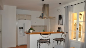 Een keuken met een koelkast, een spoelbak, een fornuis en twee barkrukken.