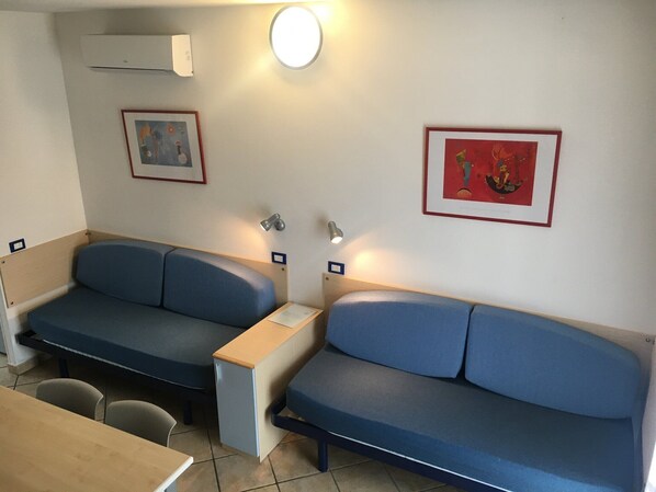A room with two blue sofas, a small table, and two wall-mounted lamps. There are framed pictures on the walls. - Relaxing Resort Apartment (Lido di Spina)