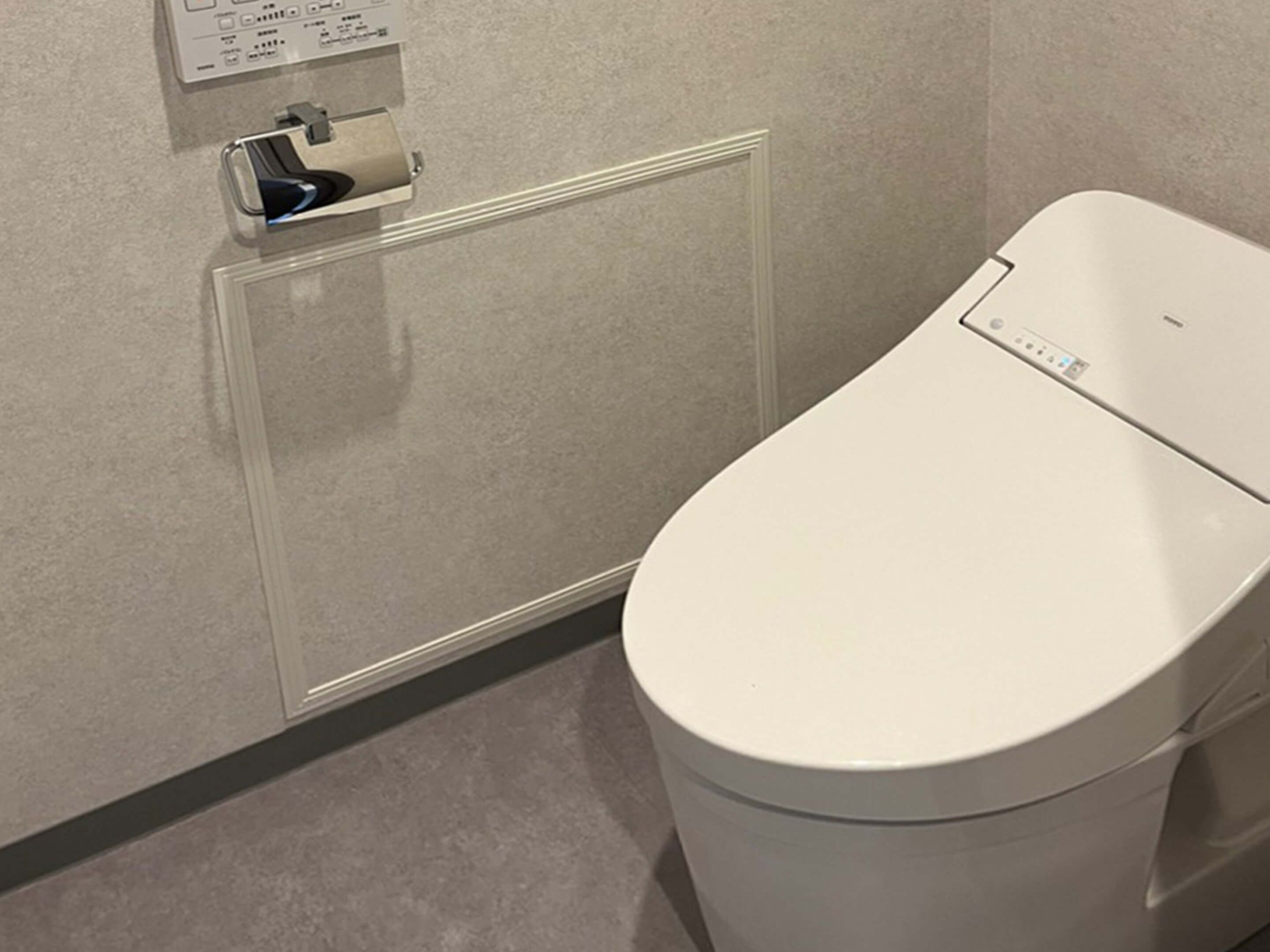 A modern bathroom with a toilet, a paper towel dispenser, and a wall-mounted control panel.