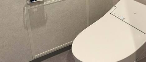 A modern bathroom with a toilet, a paper towel dispenser, and a wall-mounted control panel.