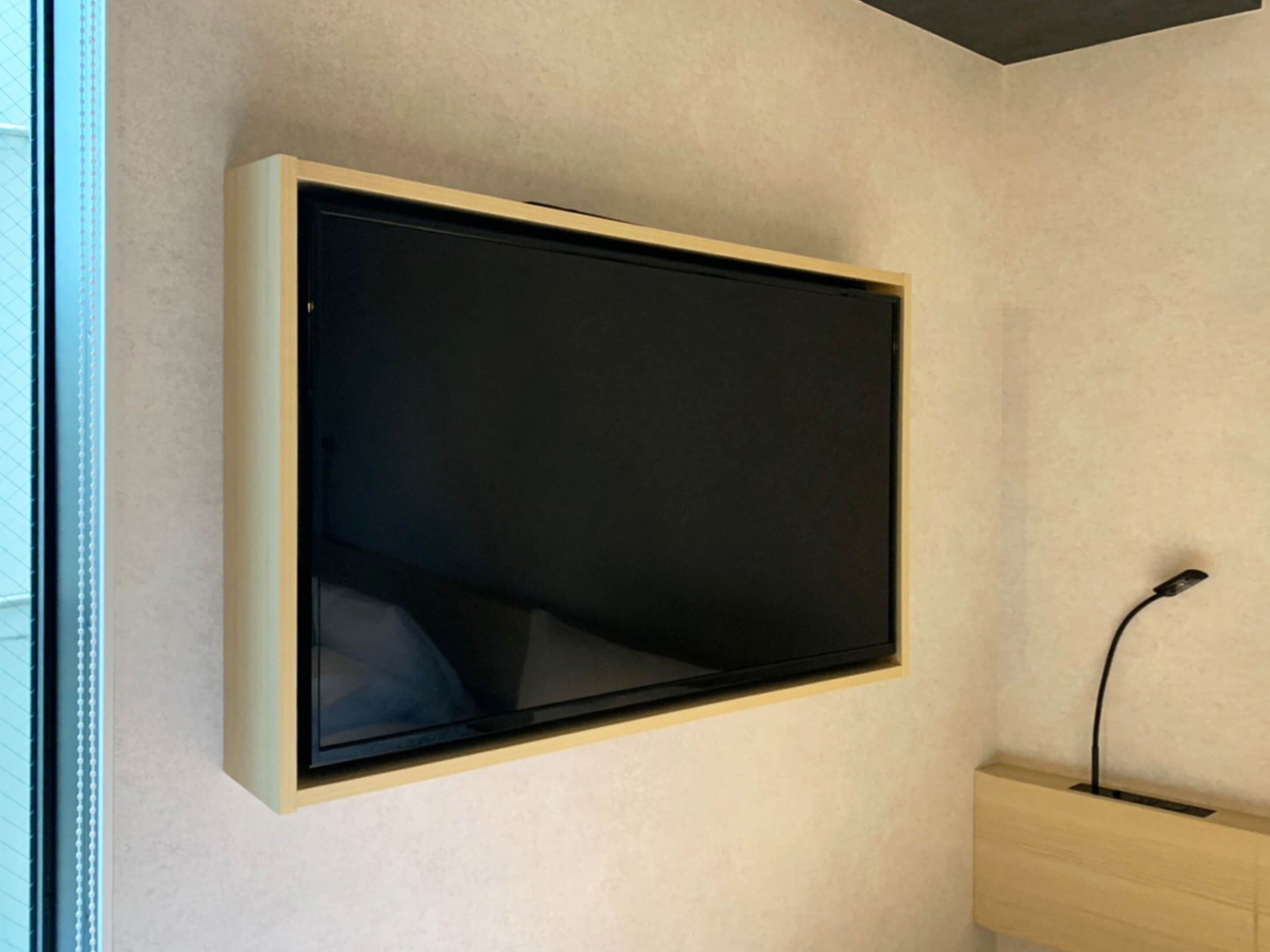 A wall-mounted television in a room with a light-colored wall and a wooden cabinet below it.