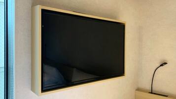 Televisão fixada na parede em um quarto com parede em tom claro e um armário de madeira abaixo.