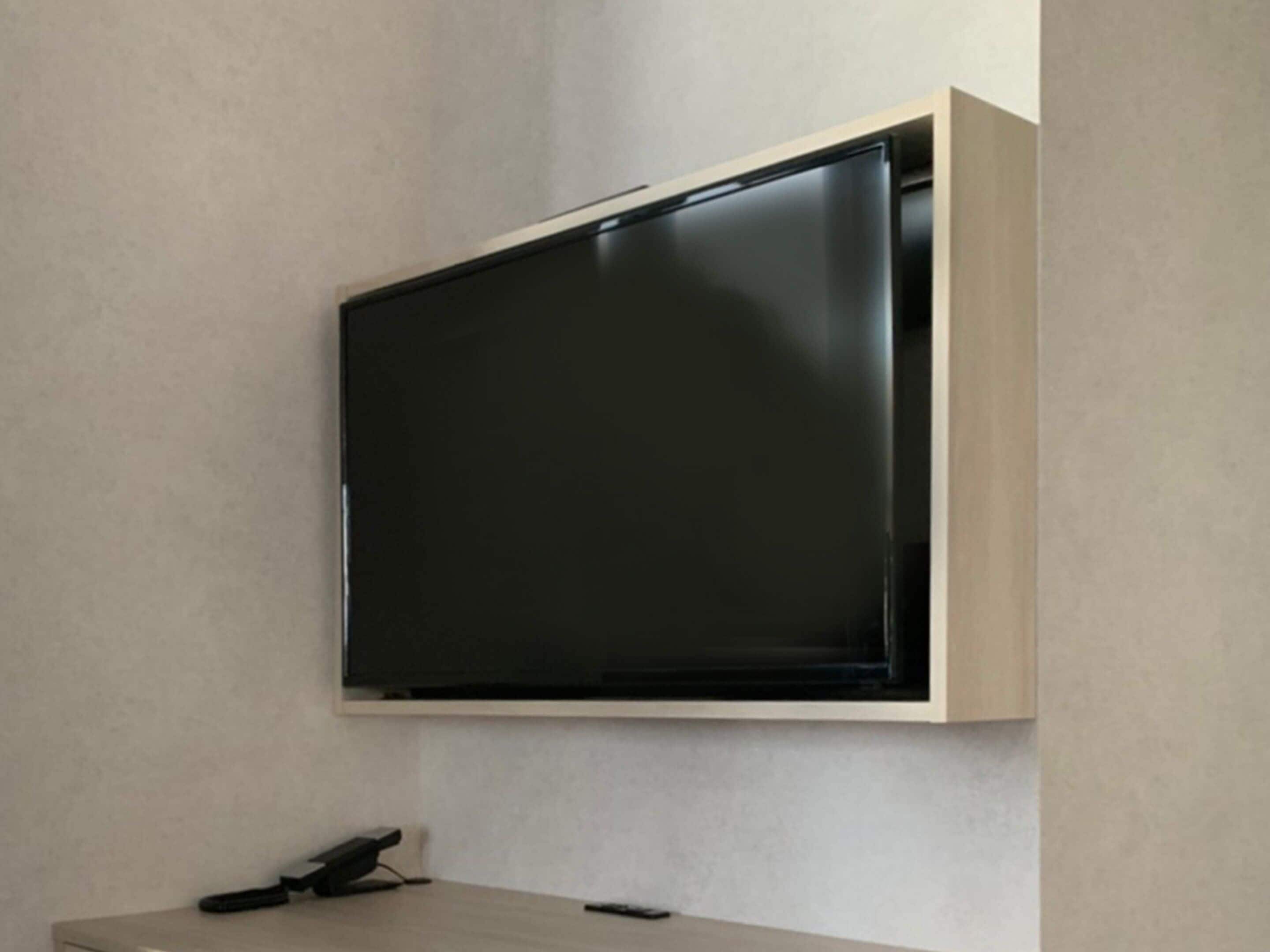 A wall-mounted flat-screen TV in a minimalist room with a wooden table and a remote control.