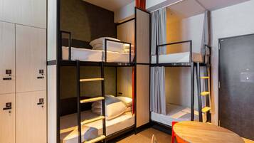 A bunk bed room with a desk and chairs, a wardrobe, and a refrigerator.