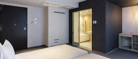 A modern hotel room with two beds, a dark accent wall, a glass shower area, and a small desk.