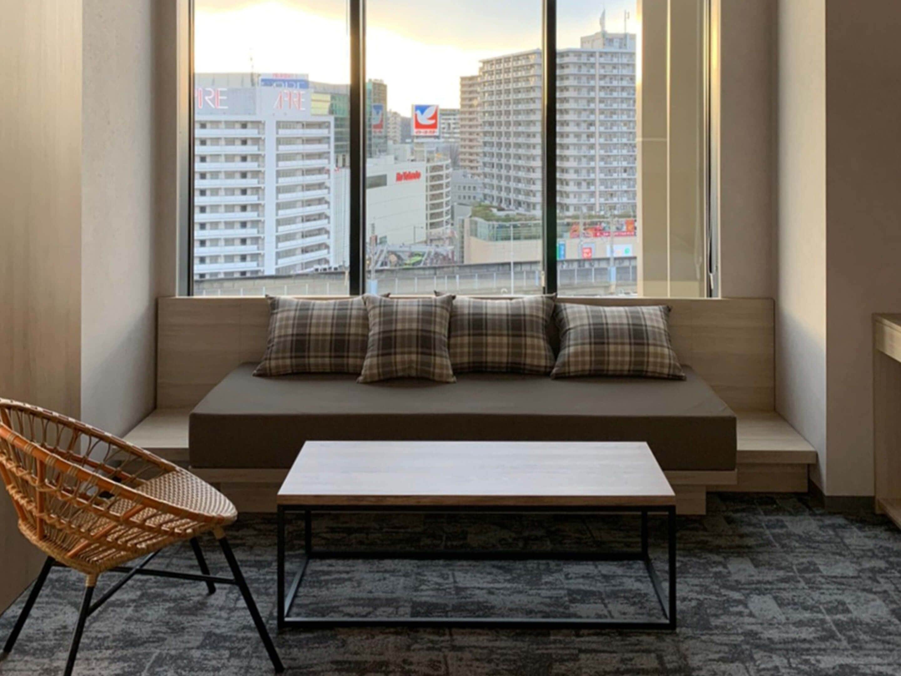 A room with a sofa, a chair, and a table near a window with a city view.