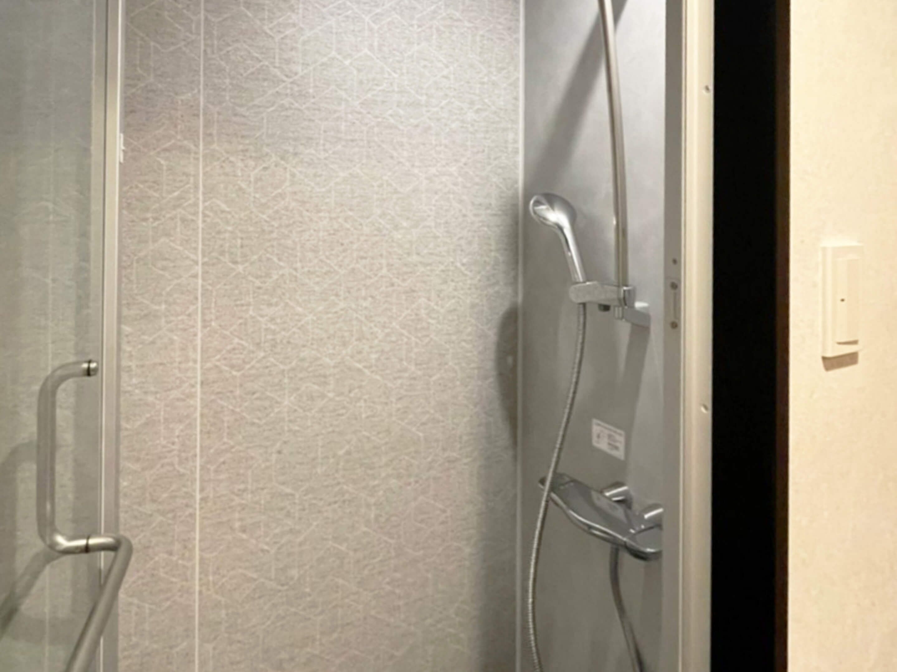 Chuveiro com porta de vidro, parede com textura e tomada elétrica aparente.