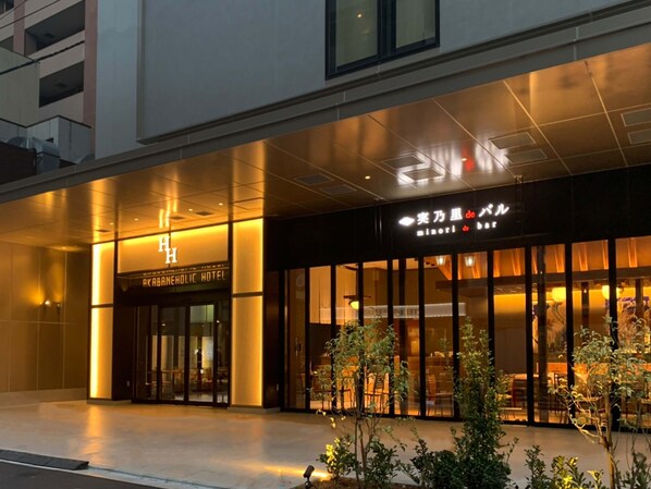 The exterior of the Akaban Hotel with a modern facade, large glass windows, and a well-lit entrance. - AKABANEHOLIC HOTEL (Tokyo)