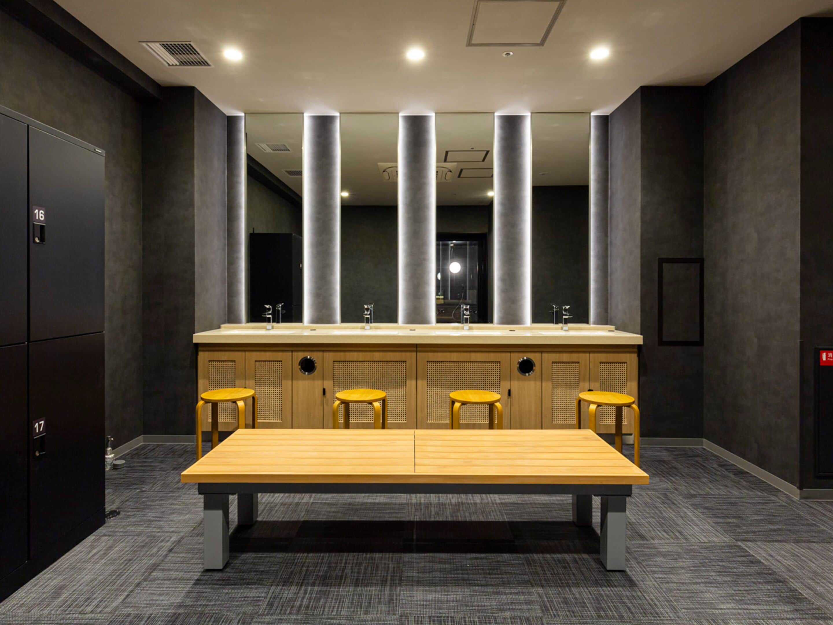 A modern restroom with a large sink, four stools, and a bench.