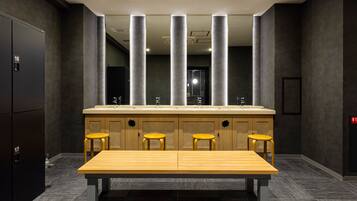 A modern restroom with a large sink, four stools, and a bench.