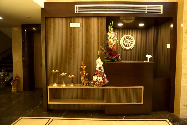 A reception desk with a decorative floral arrangement, a statue, and a wall-mounted clock. - Hotel Grand Girdhar (Indore)