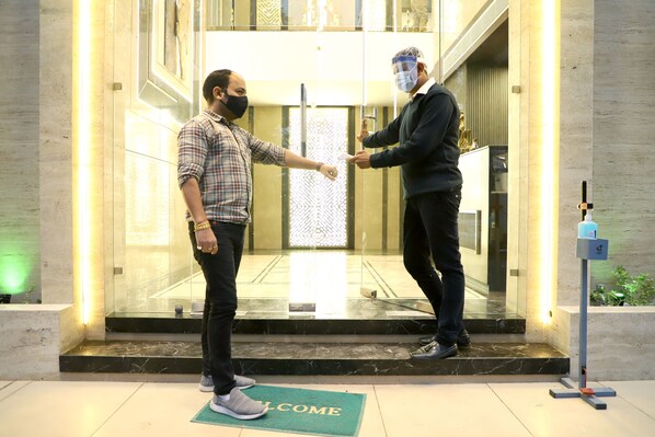 Two individuals shaking hands in a modern lobby with a marble floor and a welcome mat. - Hotel Grand Girdhar (Indore)
