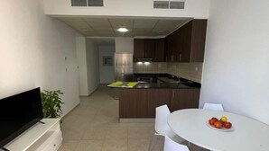 A modern kitchen with a dining area, white walls, and a flat-screen TV. - Luxury Private Room in an Apartment Next to Barasti Beach  (Dubai)