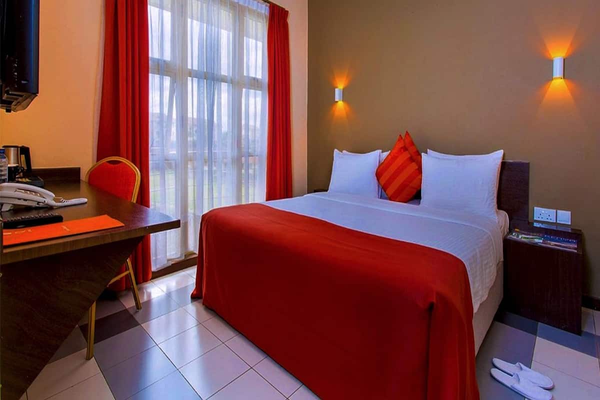A hotel room with a bed, a desk with a telephone, a chair, and a nightstand with a lamp.