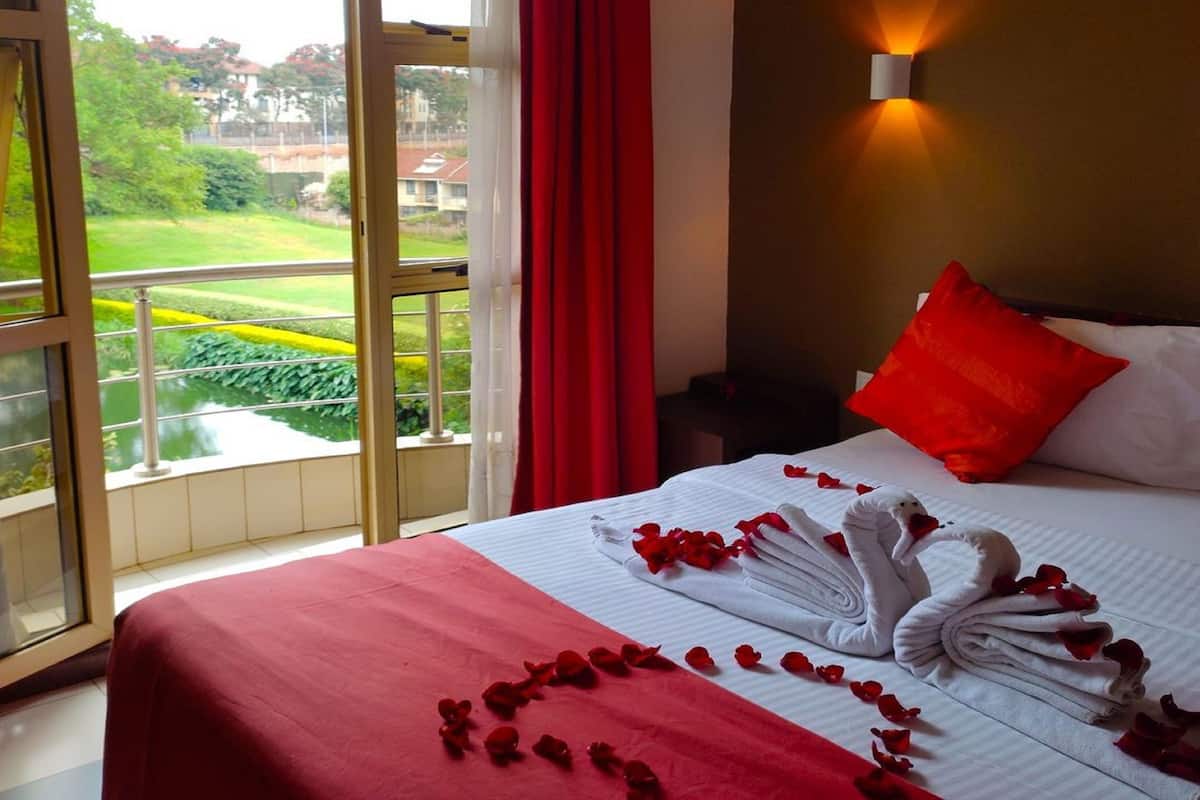 A hotel room with a balcony, a bed with red bedding, a red pillow, and a wall-mounted light.