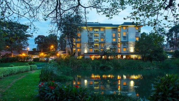 A multi-story hotel with a reflective pond in front, surrounded by greenery and trees. - Qaribu Inn Boutique Hotel Nairobi (Nairobi)