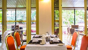 A dining area with tables set for service, large windows, and a view of greenery outside. - Qaribu Inn Boutique Hotel Nairobi (Nairobi)