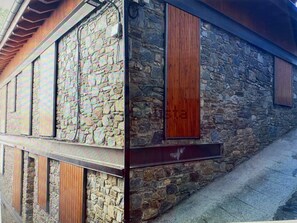 Un edificio de piedra con contraventanas de madera y fachada pétrea.