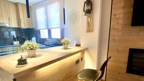 Et moderne køkken med træskabe, en central ø med vask og plantekasser, et hængende lysarmatur og en sort stol.