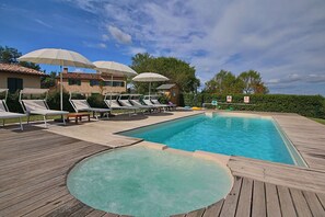 A pool area with lounge chairs and umbrellas, surrounded by a wooden deck and a clear blue sky.